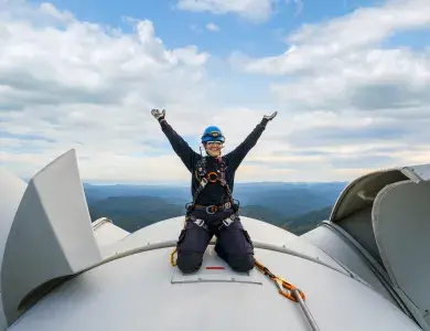 Technicienne souriante sur le toit d'une éolienne levant les mains au ciel