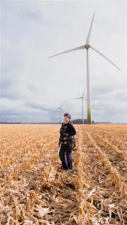 Technicienne éolien Boralex dans un champ face à une éolienne au Canada